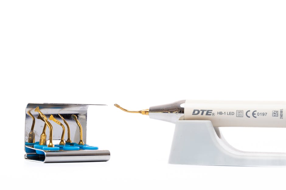 A close-up image of a dental light curing unit with a white handle and a metallic tip, positioned on a white surface. The device features the brand name 'DTE' along with technical markings, resting on a white plastic stand. To the left, six small gold-colored dental curing light tips with blue bases are aligned in a row, attached to a modern, curved metallic holder. The background is plain white, emphasizing the precision tools used in dental procedures. The scene showcases equipment typically stored in a clinical environment, with clean and sterile textures, suitable for illustrating professional dental or medical waste disposal services provided by Garbage Disposal. The arrangement and clarity suggest an emphasis on high-quality, specialised tools that may require proper handling when disposed of as part of private waste management or alternative collection methods in healthcare settings, aligning subtly with the broader context of rubbish removal and responsible waste handling.